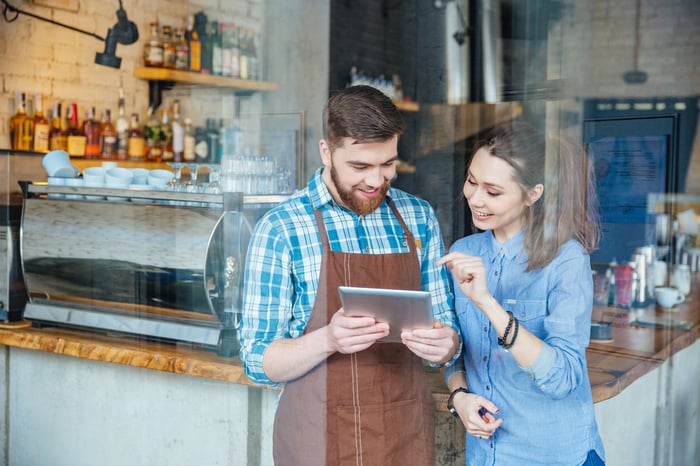 Smiling handsome waiter holding tablet and young pretty woman pointing on it in coffee shop-1